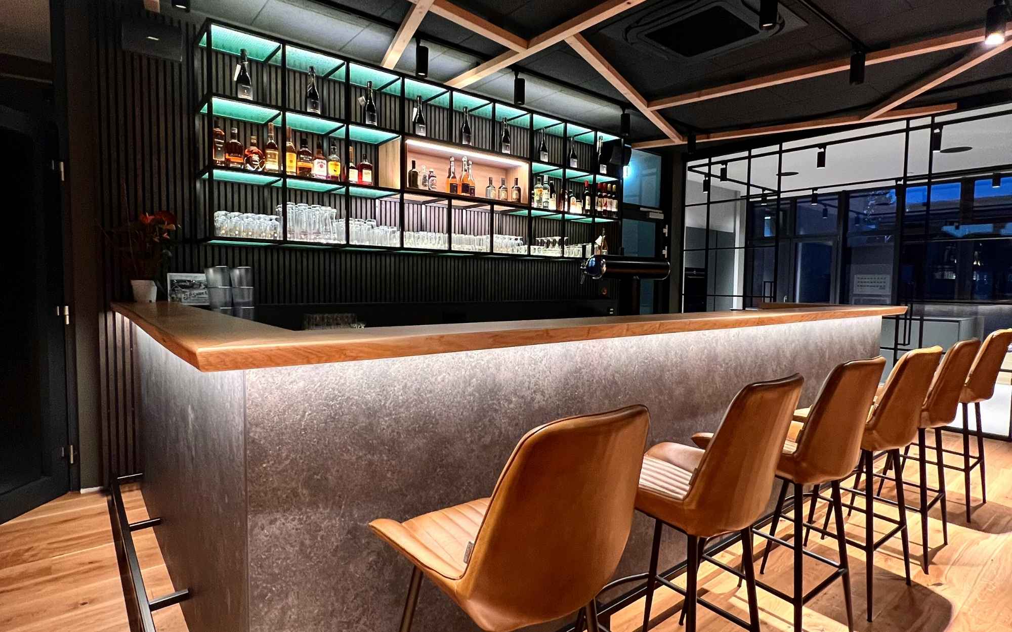 Die moderne Bar im Waidmanns mit beleuchtetem Flaschenregal und lederbezogenen Barhockern