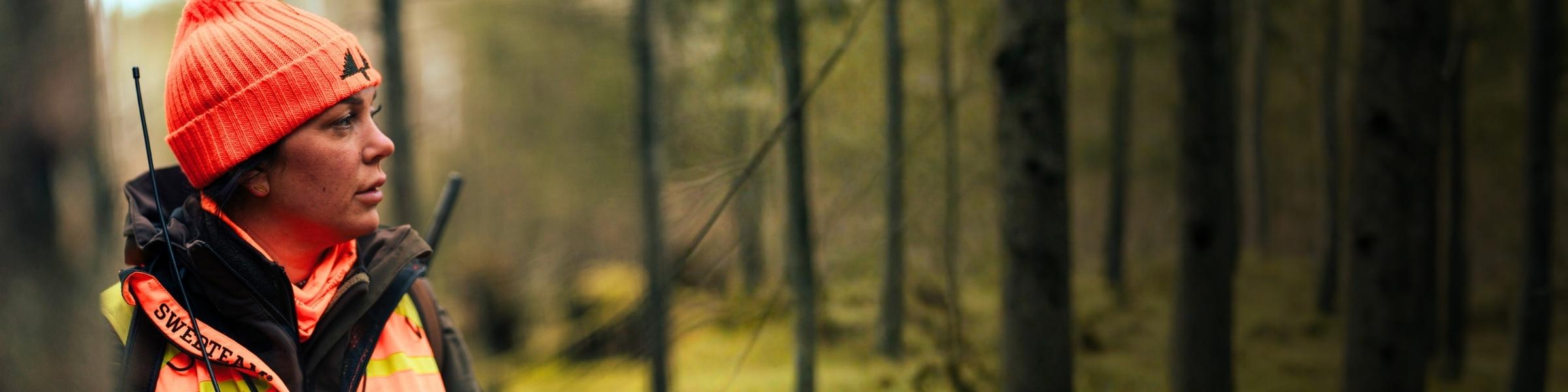 Jägerin mit orangefarbener Signalmütze im Wald
